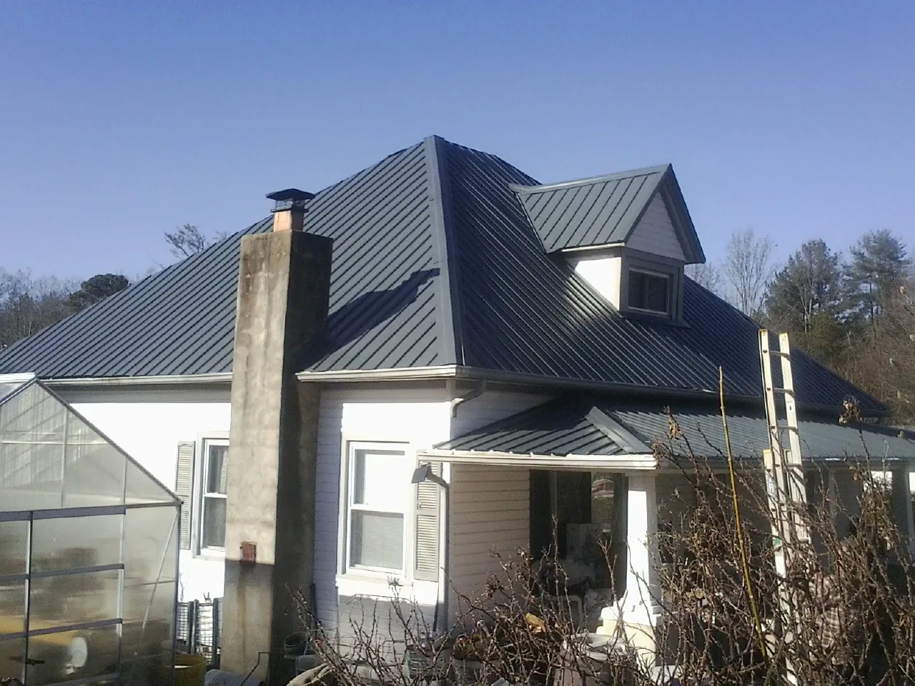 Dark blue standing seam metal roof on a white farmhouse with dormer — Slate & Tile Roof Repair by Roofing Brothers in Fort Defiance