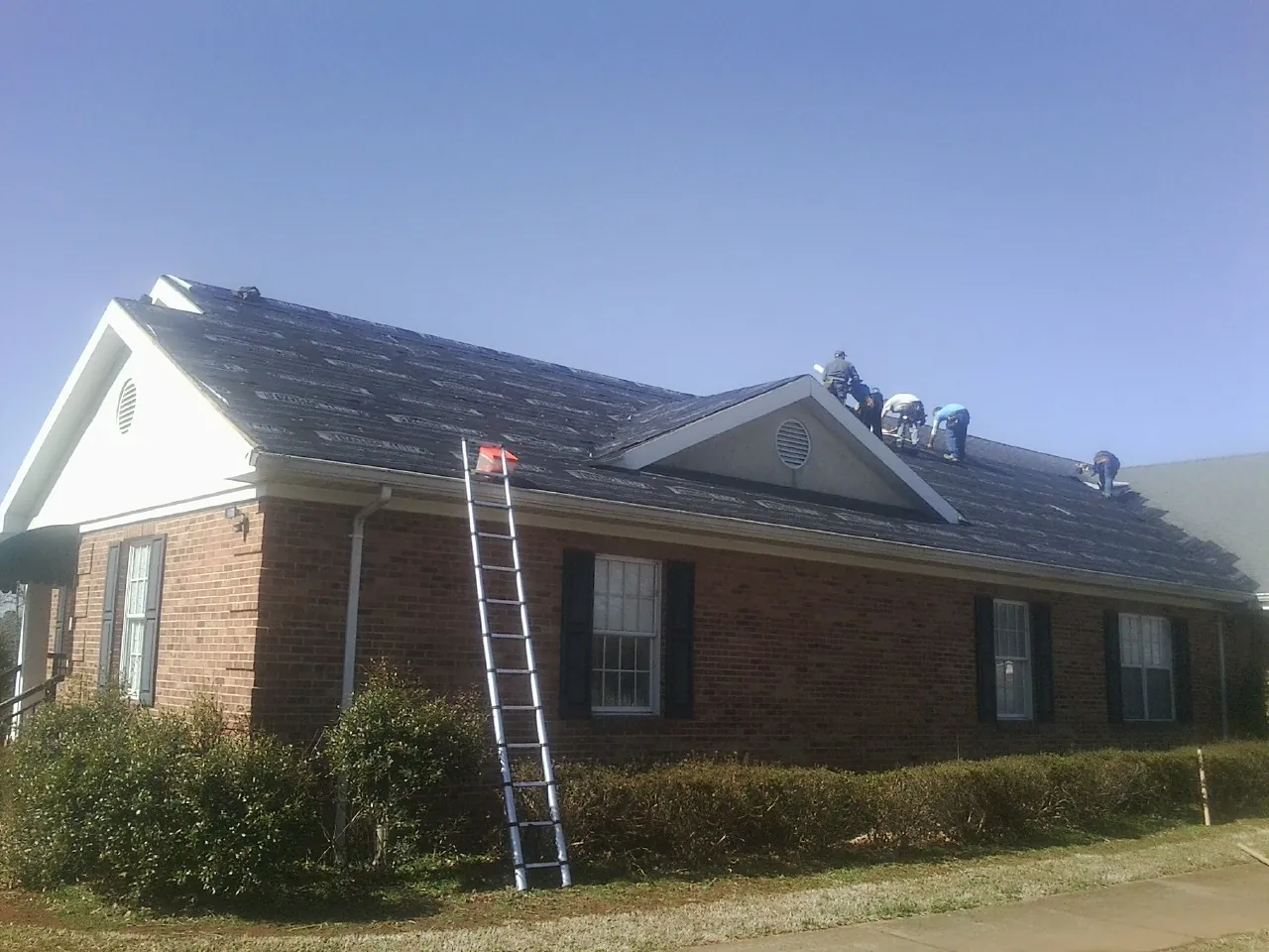 Crew tearing shingles off a brick ranch roof with a ladder set — Emergency Roof Repair work by our crew in Fort Defiance