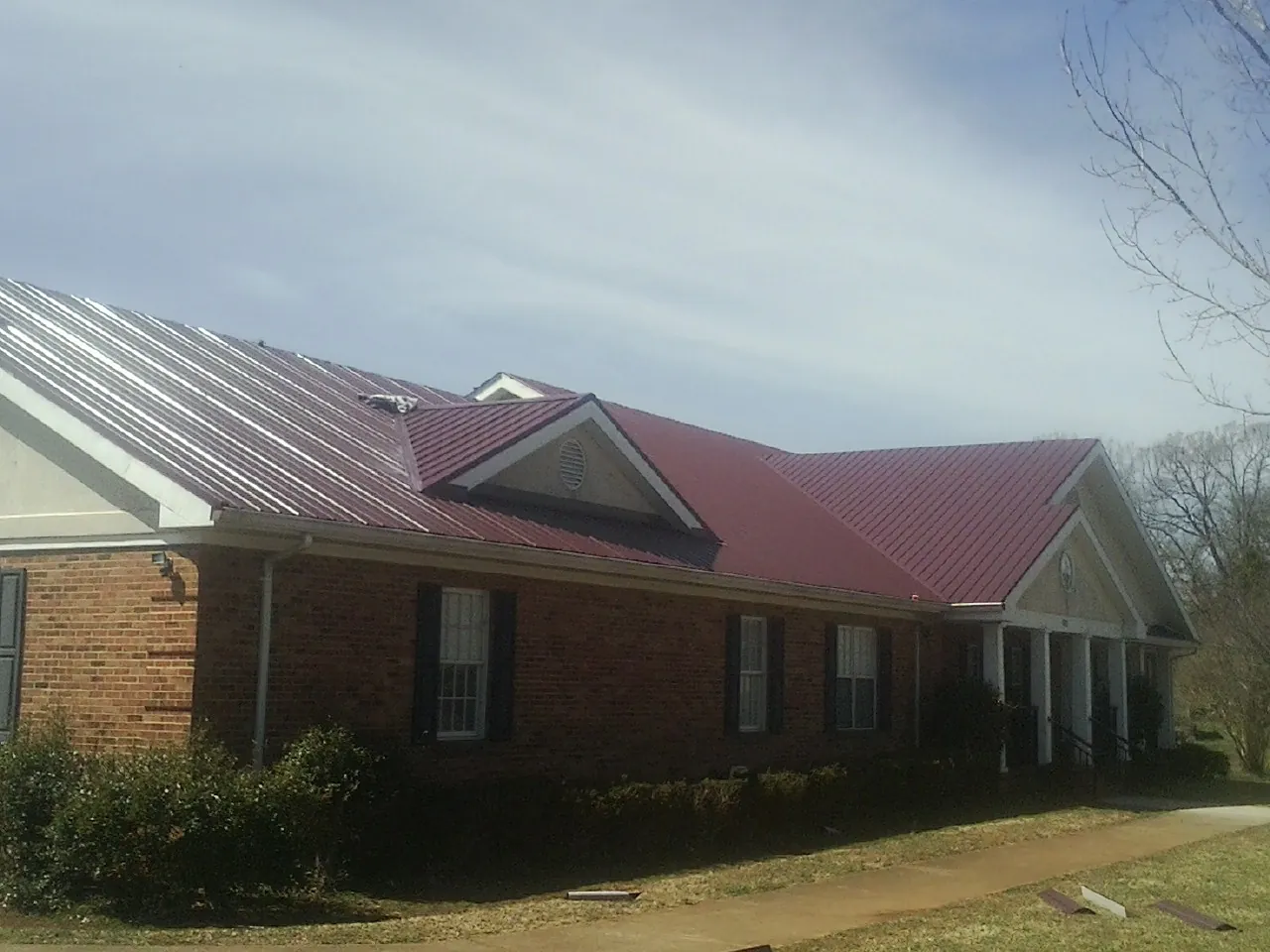 Red metal roof with gabled entries on a long brick building, from a Hail Damage Roof Repair job in Fort Defiance