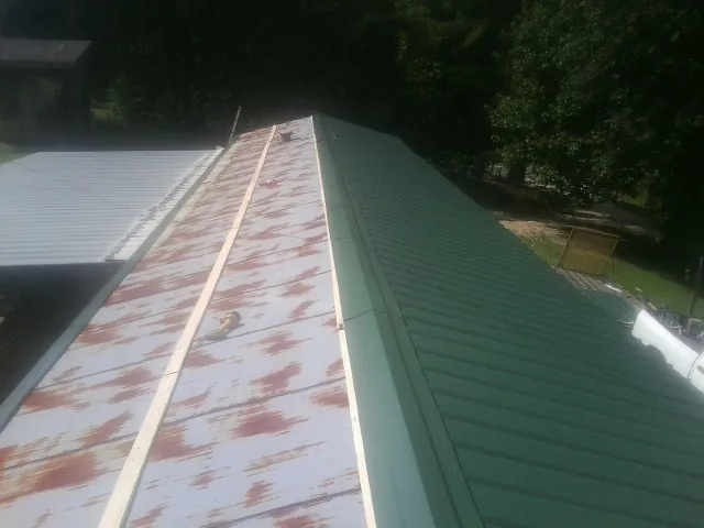 Old rusted panels beside newly installed green metal roofing — Wind Damage Roof Repair by Roofing Brothers in Fort Defiance