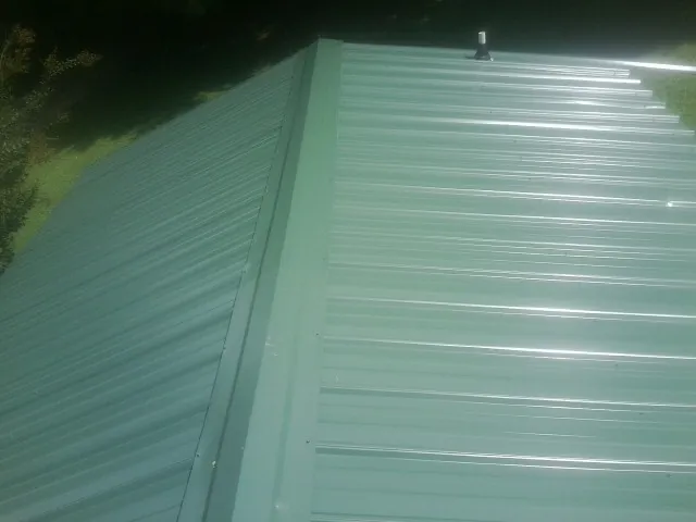 New green metal panels meeting at the ridge of a roof — Flat Roof Repair work by our crew in Fort Defiance