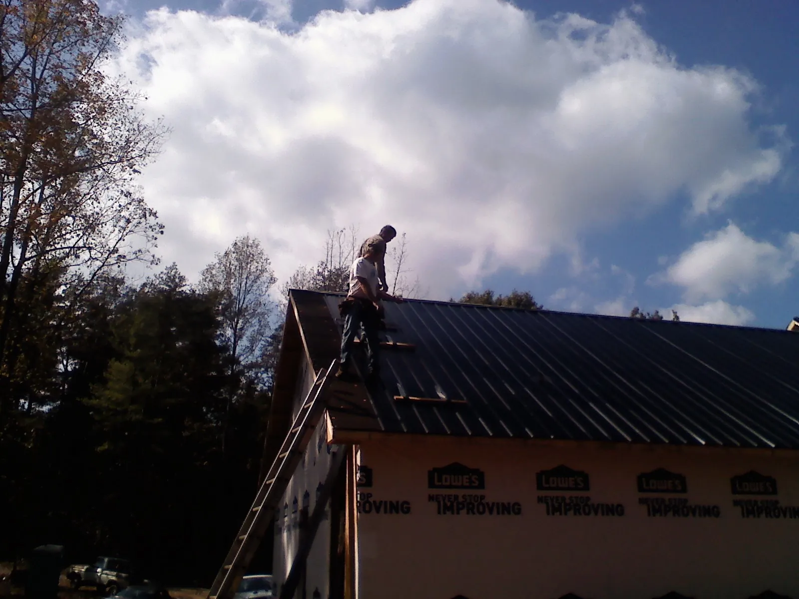 Roofer fastening dark metal panels high against a cloudy sky, from a Roof Inspection job in Fort Defiance