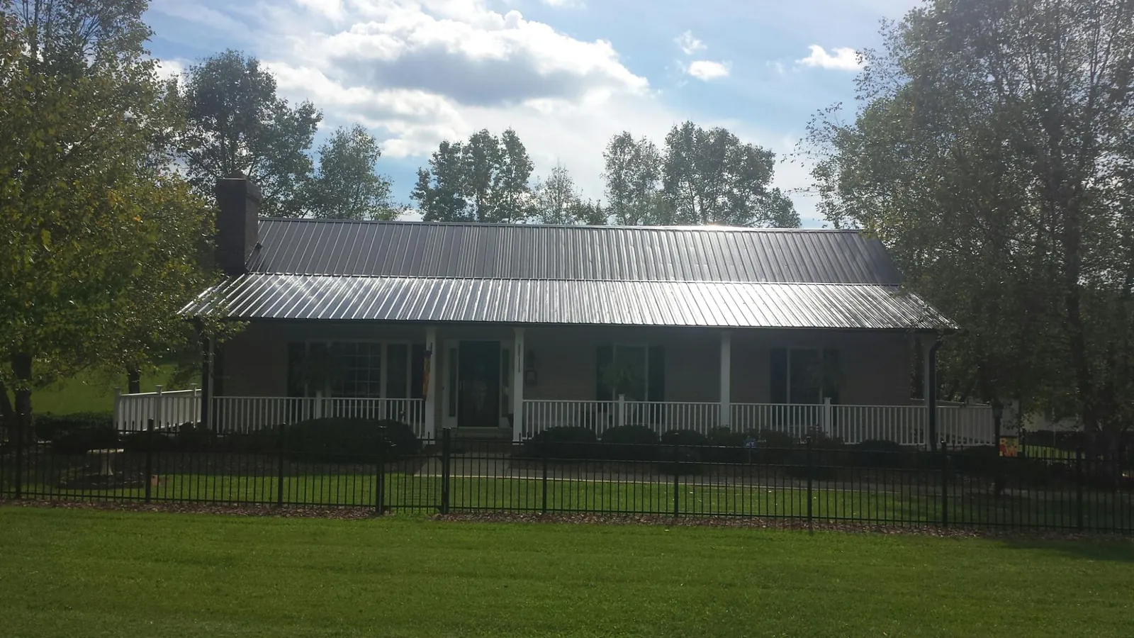 Gray metal roof on a brick ranch with a full width front porch — Gutter Guard Installation work by our crew in Fort Defiance