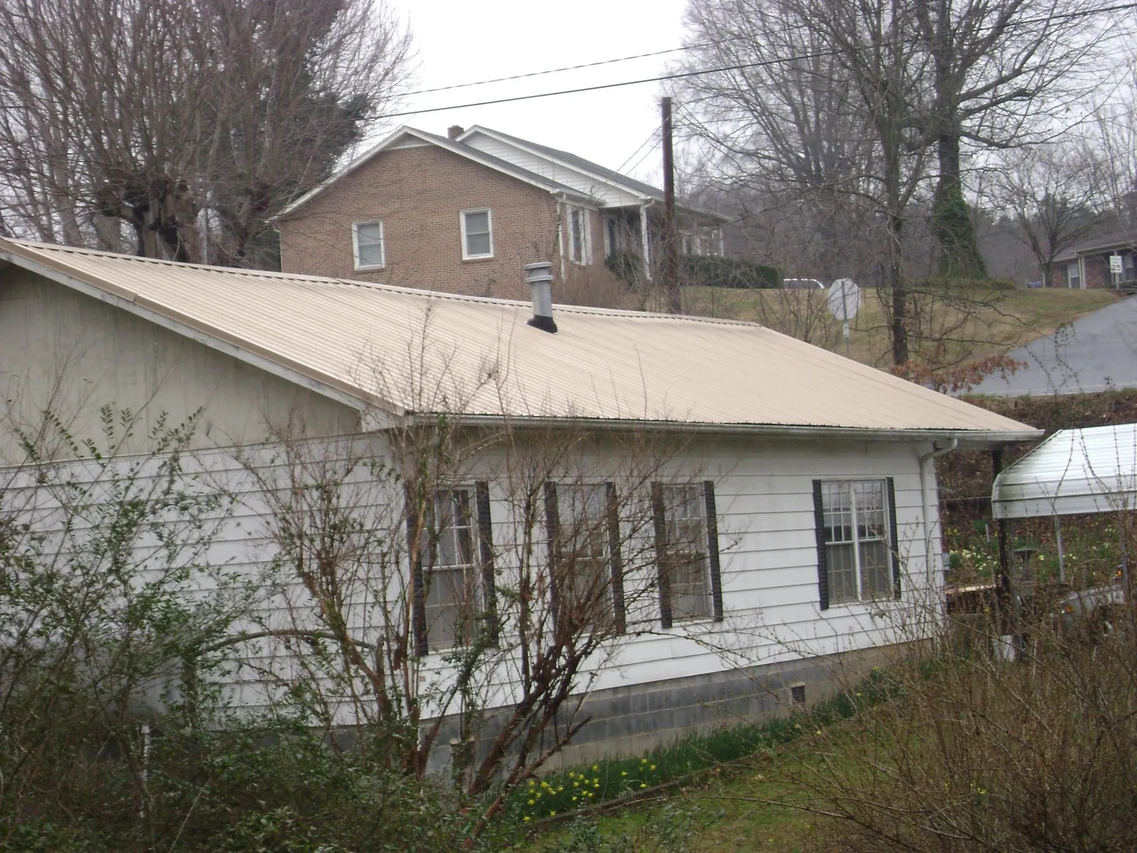 Tan metal roof on a white sided house set into a hillside — Commercial Roofing by Roofing Brothers in Fort Defiance
