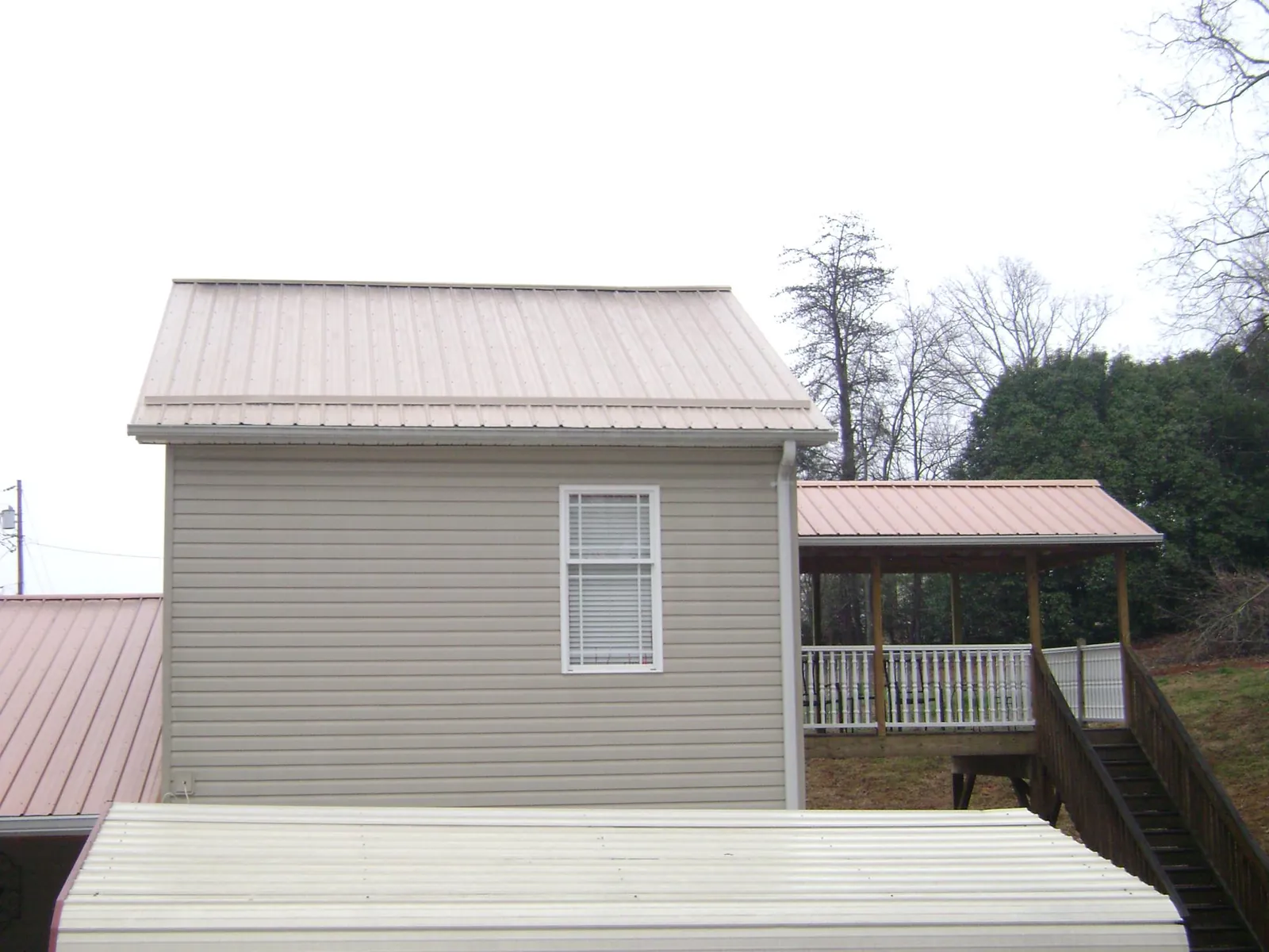 Tan metal roofs on a two story addition and attached porch, from a Roof Replacement job in Fort Defiance